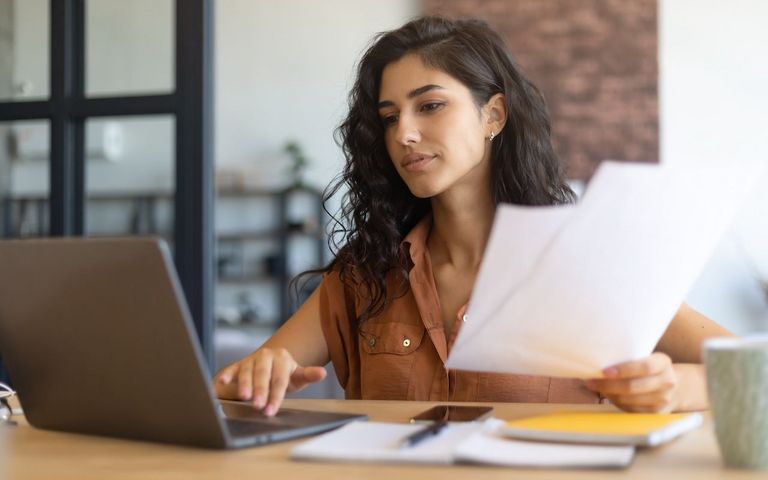 Eine Frau sitzt an einem Tisch und arbeitet mit einem Laptop. 